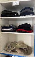 Shelving unit holding neatly folded men's sweatpants, long sleeve shirts, and workout clothes in various colors. Bottom shelf contains stacked wide-brim sun hats in light colors.