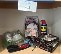 Full lot showing WD-40, smoke/CO alarm, light bulbs, hooks, and multi-tool on shelf.