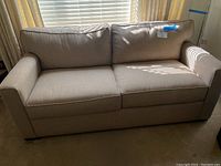 Full view of beige fabric queen sleeper sofa with two seat cushions and two back cushions, straight arms, situated in a room with window and blinds.