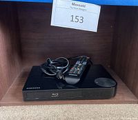 Samsung Blu-ray player inside a wooden shelf with remote and power cord on top.