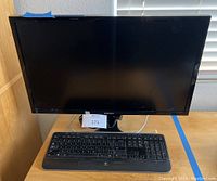 Front view of Samsung monitor and Logitech keyboard on wooden desk showing size and condition.