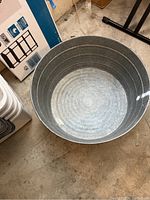Photo showing inside and top of silver galvanized metal washing bucket with rolled rim, placed on concrete floor.