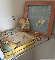 Photo showing boxed blue embroidered baby blanket, packaged baby booties, and part of the outfit and wooden toy.