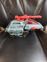 Side view of GI Joe Cobra H.I.S.S. Tank showing grey mechanical body, continuous treads, and red mounted turret gun.