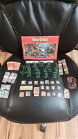 Full set displayed on chair including box cover, miniatures, game tiles, cards and tokens