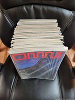 Stack of 35 Omni magazines viewed from the top edge showing pages and thickness, seated on a black leather chair.