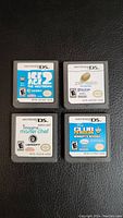 Front view of four Nintendo DS game cartridges arranged in a 2x2 grid on a black surface. Titles are Ice Age 2 The Meltdown, Zenses, Imagine Master Chef, and Club Penguin Herbert's Revenge.