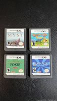 Front view of four Nintendo DS game cartridges placed on black leather surface showing label artwork for Myst, SpongeBob Drawn to Life, World Championship Poker, and Brain Age 2.