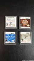 Four Nintendo DS game cartridges laid out on a black surface showing front labels of Imagine Fashion Designer, Texas Hold'em Poker, Brain Age 2, Brothers in Arms DS.
