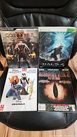 Lot overview of four video game strategy guides on black chair: God of War 2, Halo 4, Disney Infinity 2.0, Resident Evil 2.