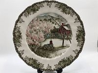 Photo showing entire front of the vintage ceramic plate with scenic village motif and decorative border.
