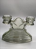 Clear pressed glass double candle holder with ribbed base and decorative arch between two candle cups, photographed against white background.