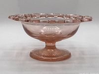 Front-side view showing pink depression glass bowl with ornate open lace edge and pedestal base.