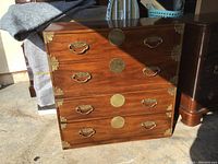 Front view of two stacked Asian campaign chests made of solid wood with brass hardware, showing two drawers each with brass handles and central circular plates, and brass corner protectors.
