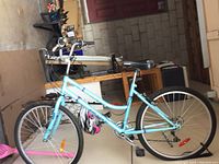 Side view of turquoise women's bicycle showing step-through frame, black seat, front and rear wheels and handlebar details.