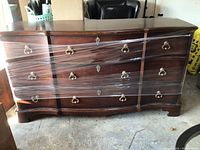 Front view of the large dark wood dresser wrapped in plastic, showing three rows of drawers with metal handles.