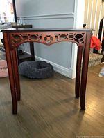 Photo of the entrance table showing decorative wood cutouts below tabletop and curved tapered legs on hardwood floor near the wall.