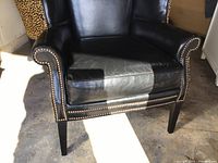 Front view of black leather wingback chair with rolled arms and nailhead trim on wooden legs