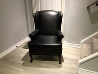 Front view of the black leather wingback chair on wooden floor showing condition and style.