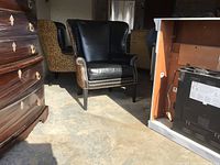 Front three-quarter view showing overall chair design, black leather seat, rolled arms, nailhead trim and wooden legs
