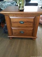 Front view of one golden oak nightstand showing two drawers with oval metal pulls and finished wood grain surface.