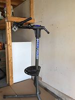 Full view of Park Tool bicycle repair stand with clamp attached, showing metal frame, clamp mechanism, and handle in a garage setting.