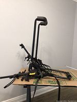 Full view of Saris bike carrier rack folded on cardboard surface showing vertical support bars, straps, and bike holding arms.