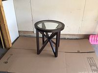 Photo of round side table with glass top, showing geometric wooden base and overall structure from a side angle.