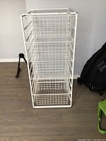 Front view of white metal storage unit with five wire baskets inside a white grid frame.