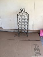 Front view of metal wine rack showing circular bottle holders arranged vertically in a single column with a decorative scroll top.