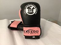 Pair of black and pink woman's kickboxing gloves with 'Total Female Kick Boxing TFK' logo and 'EXEED Going Beyond' wrist strap branding