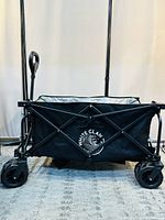 Front view of the White Claw foldable beach wagon showcasing the collapsible metal frame, black fabric with logo, and four large wheels.
