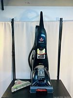 Full front view of Bissell ProHeat carpet cleaner vacuum with attached hose and clear nozzle accessory placed in front.