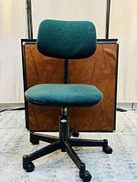 Front view of green upholstered rolling office chair showing seat, backrest, five caster base and height adjustment lever.
