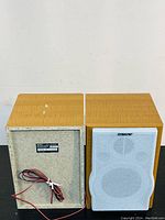 Front and back view of the bookshelf speakers showing wood grain finish, white front speaker covers with Sony logo, and back panel with label and speaker wires.