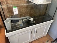 Full view of the aquarium tank on the white wooden stand with some filtration components inside the tank.