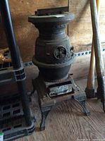 Side view of cast iron pot belly wood stove on wooden floor near tools
