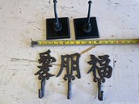 Photo of five metal wall hooks on a wooden surface, with a measuring tape showing approximately 11 inches for scale.