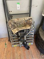 Photo of older model single person hunting tree stand with camouflaged padded seat and screw-in foot pegs.