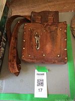 Close-up view of the front of a vintage leather toolbelt showing pouches, metal rivets, and a metal hook.