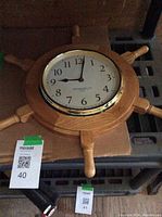 Nautical wooden wall clock on a dark surface, showing full clock face and 8 handles of ship's wheel shape.