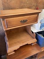 Front angled view showing drawer, open shelf and detailed molding of the wooden nightstand.