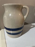 Front view showing white ceramic pitcher with blue stripes and handle