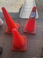 Three orange traffic pylons on a wooden surface showing square bases and tapered cones.