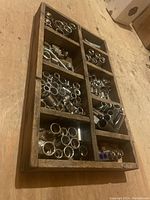 Top-down view of wooden tray containing sockets and bolts arranged in compartments on a wooden surface.