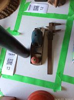 Wooden hand plane and metal caliper laid out inside a green tape square on a table, showing relative size and condition.