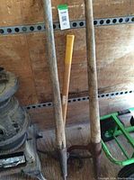 Three tools leaning against wall: one pickaxe in center, two log rolling hooks on either side