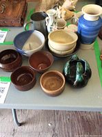 Top view of assorted bowls and vases on gray table including blue large vase, brown and beige bowls, and green decorative piece