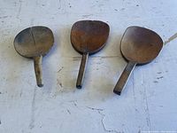 Three vintage wooden butter spoons laid flat on a white surface showing varying shapes and condition
