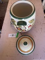 Top view of ceramic jug with removable lid placed beside it, showing interior and fruit design on exterior.